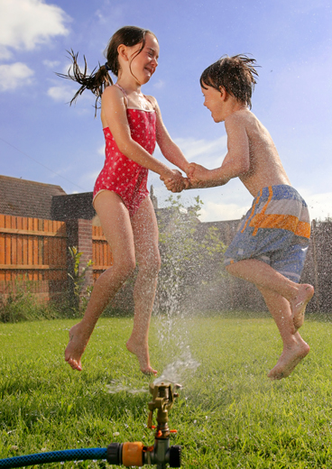 girl and boy preschoolers playing in water sprinkler