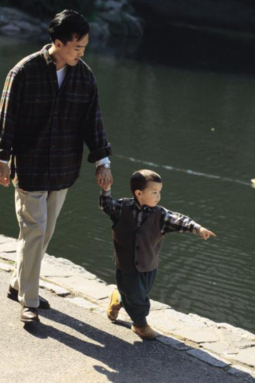 dad and preschool boy walking by  a river